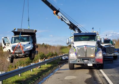 Sullivan's Towing & Recovery using a crane to lift a dump truck from the side of the road